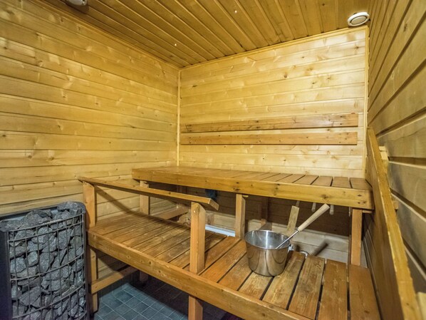 Una sauna con paredes y bancos de madera, un cubo de metal y una pared de piedra.