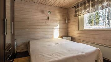 Een slaapkamer met een bed, houten wanden, een raam met uitzicht op bomen en een radiator.