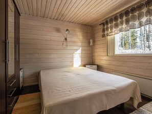 Un dormitorio con cama, paredes de madera, ventana con vistas a árboles y un radiador.