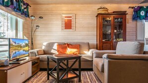 Un salon chaleureux avec un canapé, un fauteuil et une petite table basse. On y trouve un téléviseur posé sur un meuble en bois, ainsi qu'un panneau décoratif accroché au mur.