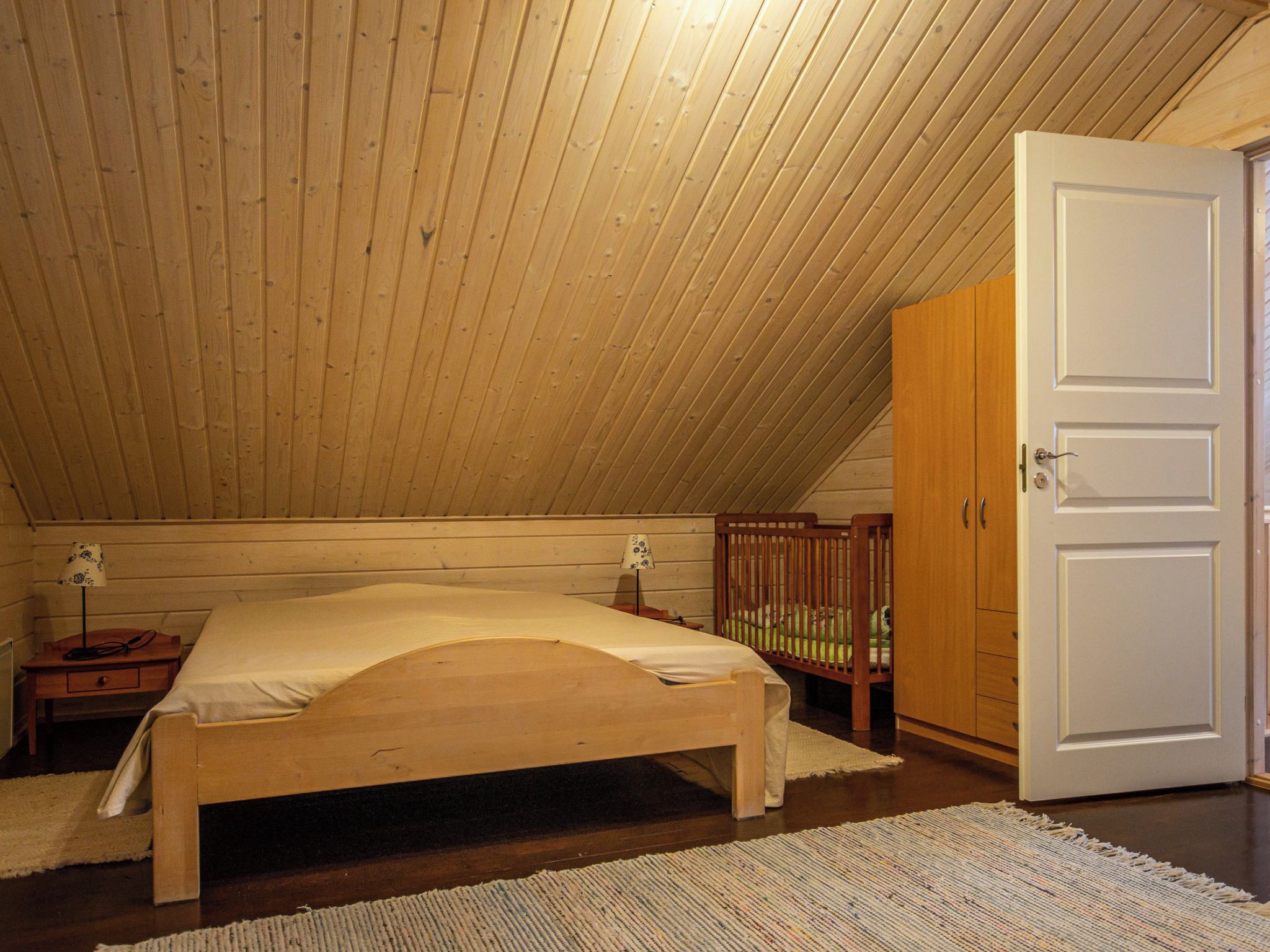 Een slaapkamer met een houten plafond, een enkel bed, een nachtkastje, een babybedje en een kledingkast.