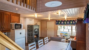 L’intérieur d’un chalet accueillant, avec une cuisine, une cheminée, un coin repas et une fenêtre avec des rideaux.