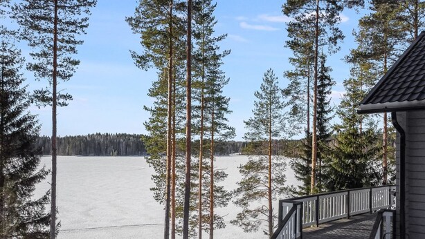 Une cabane en bois avec un escalier menant à une terrasse, entourée de grands pins et d’un paysage enneigé.