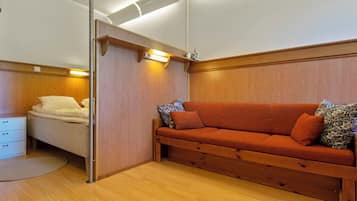 Een kamer met een houten vloer, een bank met gestreepte kussens, een bed met wit beddengoed en een bijzettafeltje met lades.