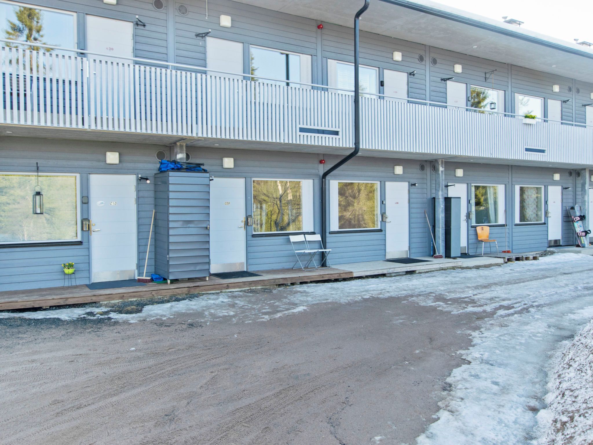 A multi-story building with a balcony on the upper floor, a covered outdoor area, and a parking lot with snow.