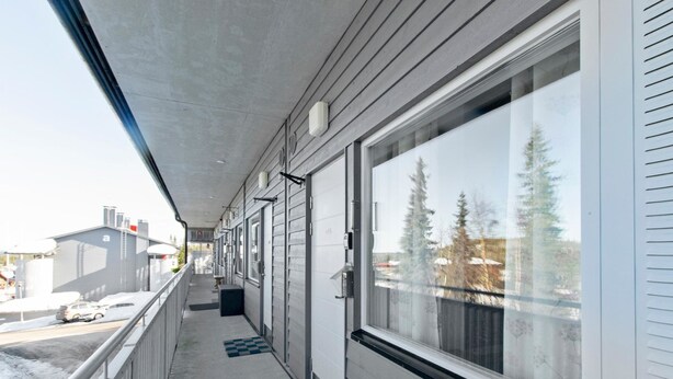 Ein überdachter Balkon mit Blick auf Bäume und ein Gebäude im Hintergrund.