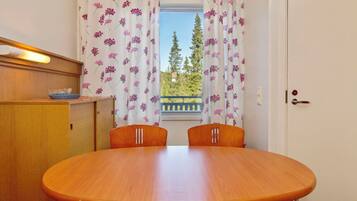 A dining area with a wooden table and chairs, a window with curtains, and a view of trees and a building outside.