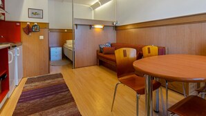 Ein kompakter Wohnraum mit Küchenzeile, einem Essbereich mit Tisch und Stühlen, einer Couch und einem kleinen Bett.