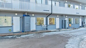 Ein zweigeschossiges Gebäude mit einem Balkon im oberen Stockwerk, einem überdachten Eingang und einem mit Schnee bedeckten Gelände.