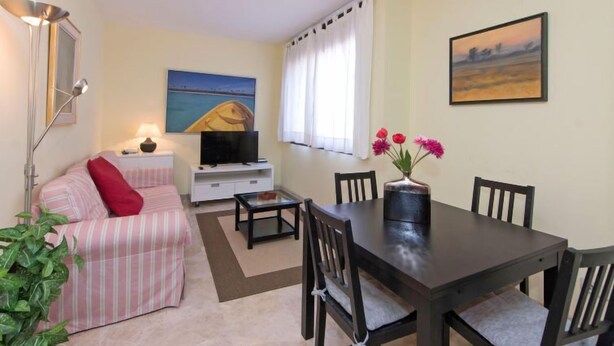 A living room with a sofa, TV, dining table, chairs, and a painting on the wall. - Vila Olímpica: Sant Martí - Sardenya by Interhome (Barcelona)