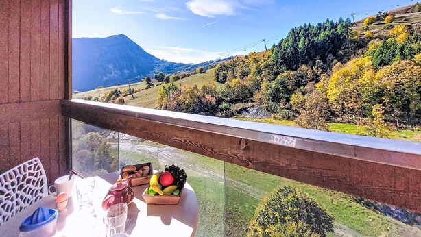 A balcony with a table set for two, overlooking a scenic landscape with hills and a mountain. - Vostok Zodiaque by Interhome (Le Corbier)