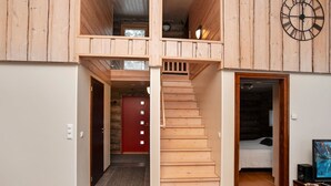 Un intérieur en bois avec un escalier menant à une mezzanine, une porte rouge et une horloge au mur.
