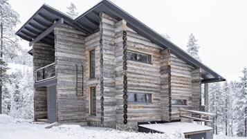 A log cabin with a balcony, large windows, and a stone foundation.