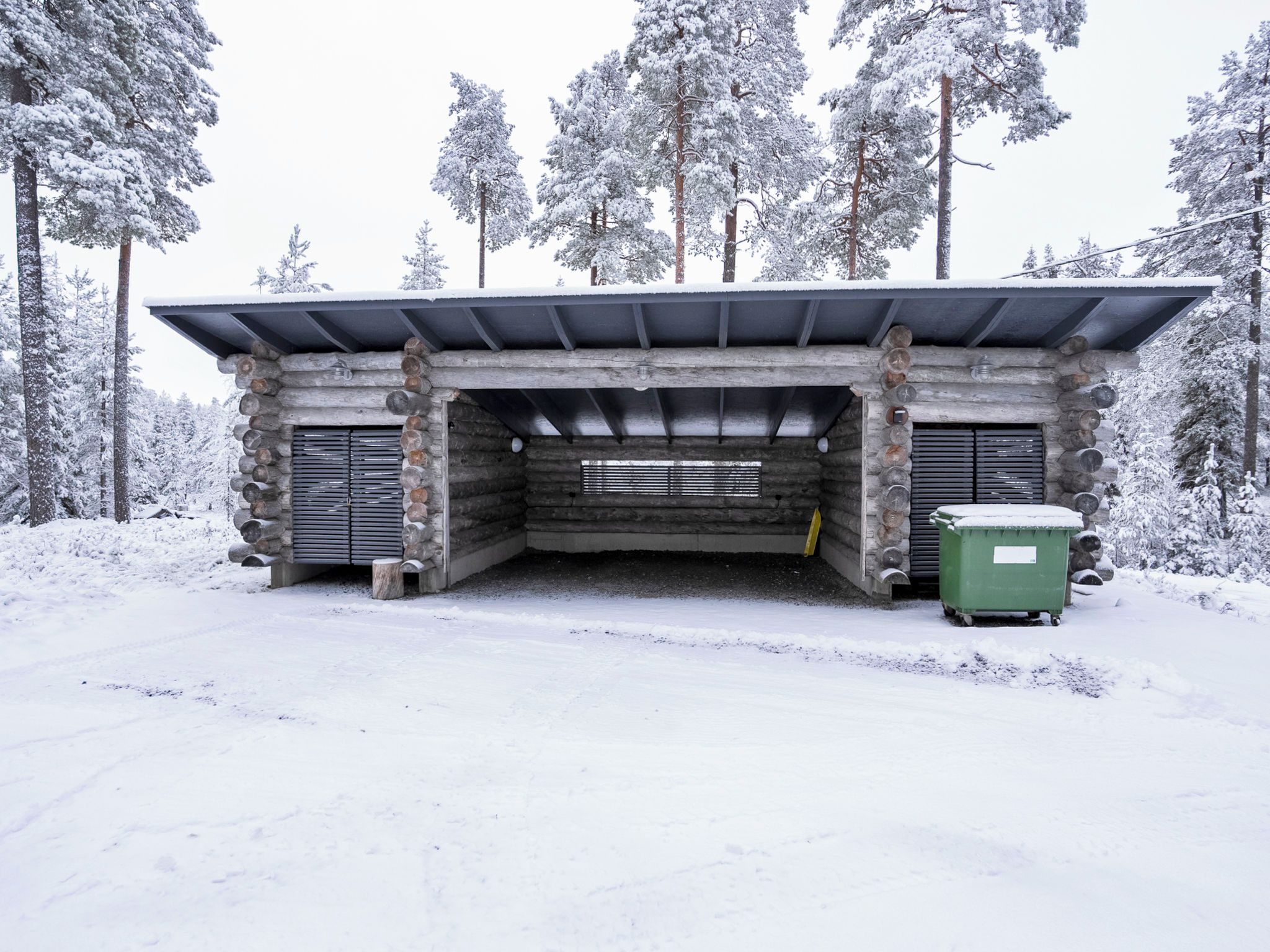 A log cabin with a metal roof, a central door, and a green dumpster outside.
