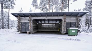 A log cabin with a metal roof, a central door, and a green dumpster outside.
