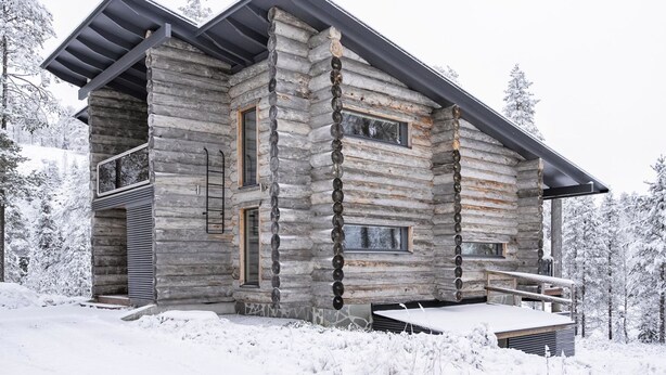 Une cabane en rondins dotée d’un balcon, de grandes fenêtres et surplombant un paysage enneigé.