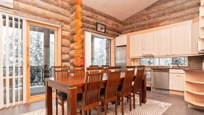 L’intérieur d’une cabane en rondins comprend un coin repas, une cuisine et des portes-fenêtres coulissantes qui donnent sur une terrasse extérieure enneigée.