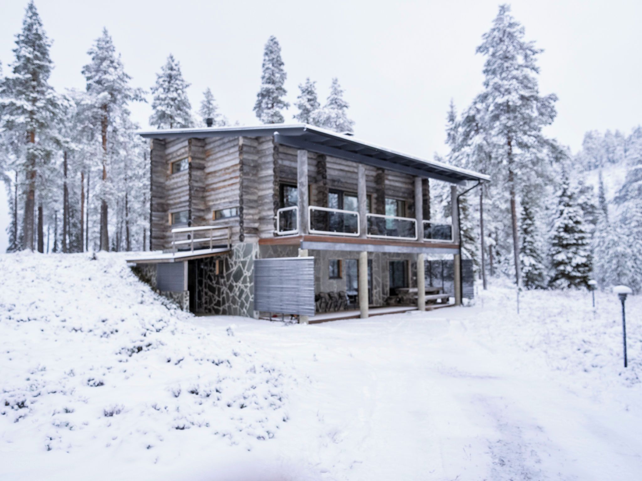 A log cabin with a balcony, surrounded by snow-covered trees.