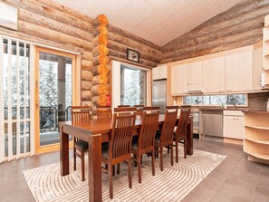 L’intérieur d’une cabane en rondins comprend un coin repas, une cuisine et offre une vue sur des arbres couverts de neige.