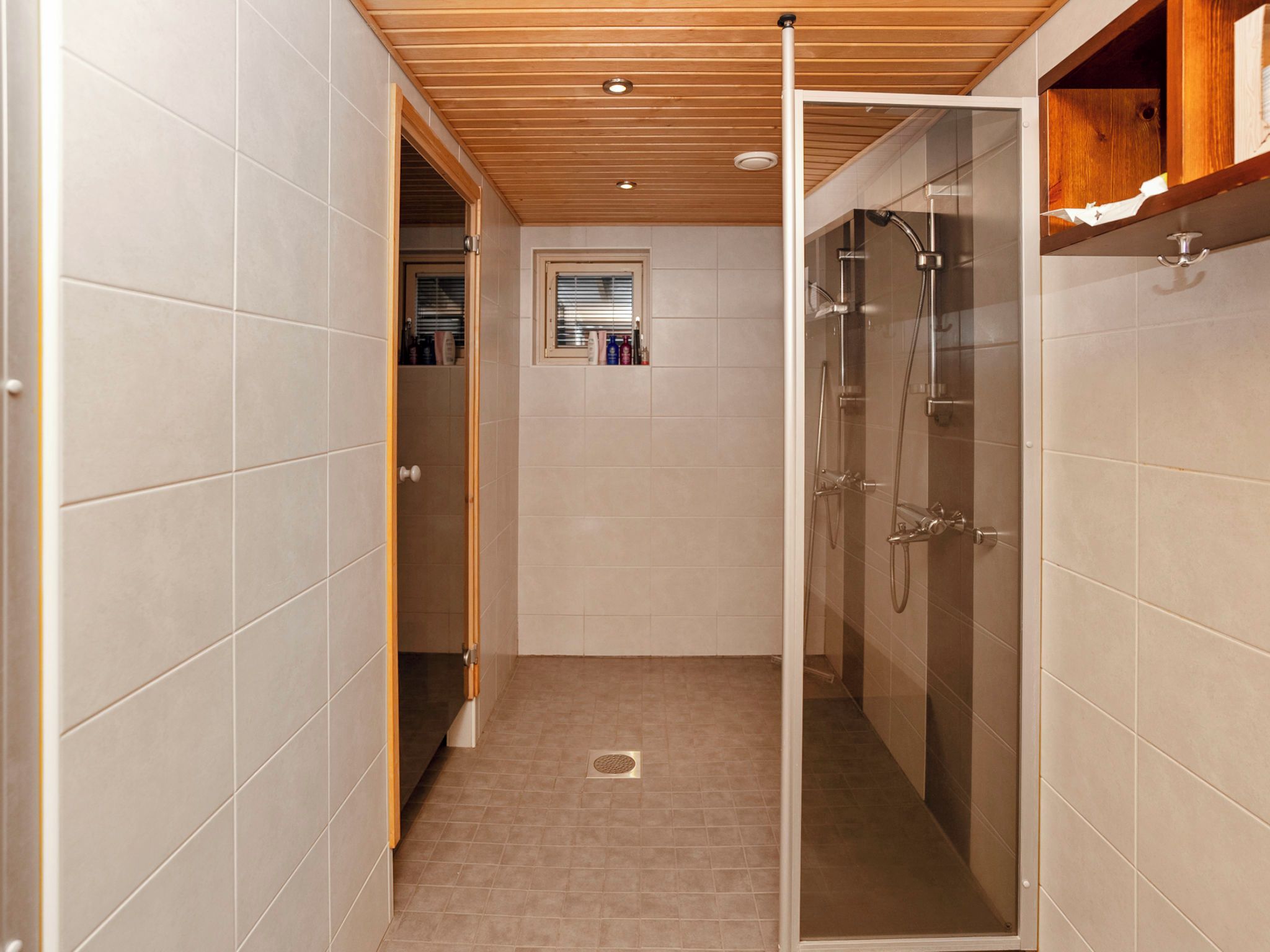 A modern bathroom with a glass-enclosed shower, tiled walls, and a wooden ceiling.