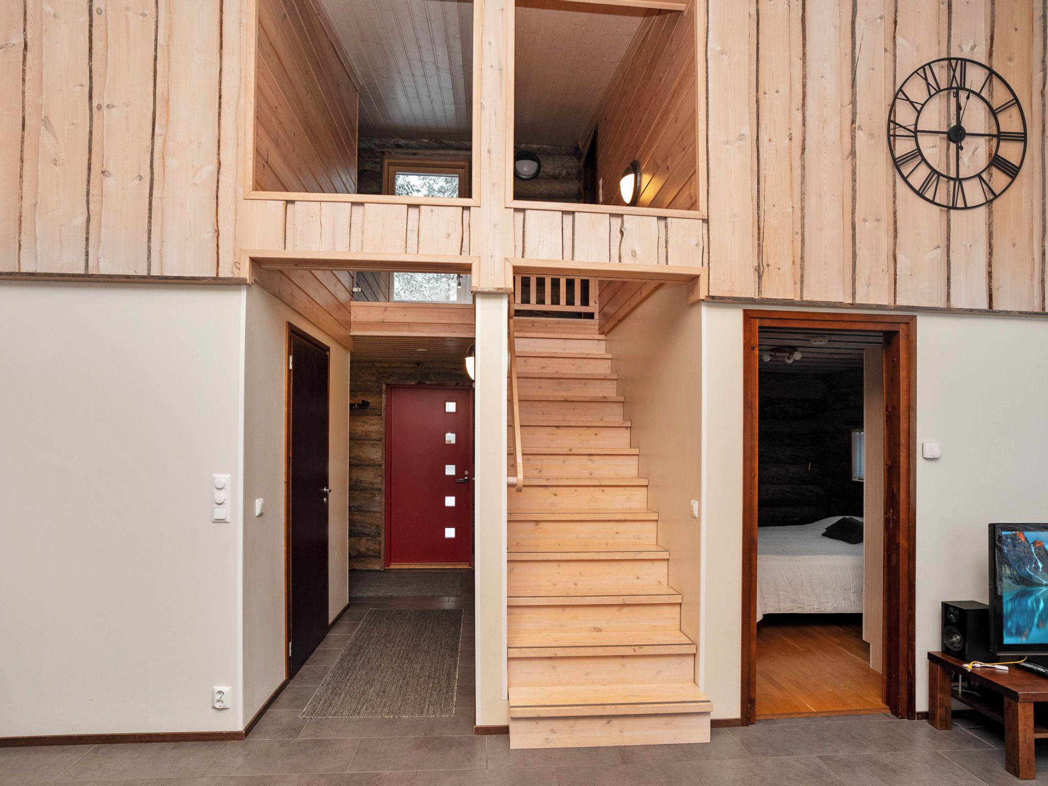 A multi-level wooden interior with a staircase, a red door, and a clock on the wall.
