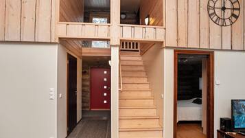 A multi-level wooden interior with a staircase, a red door, and a clock on the wall.