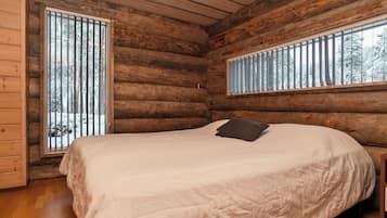 A log cabin bedroom with a bed, two windows, and a wooden ceiling.