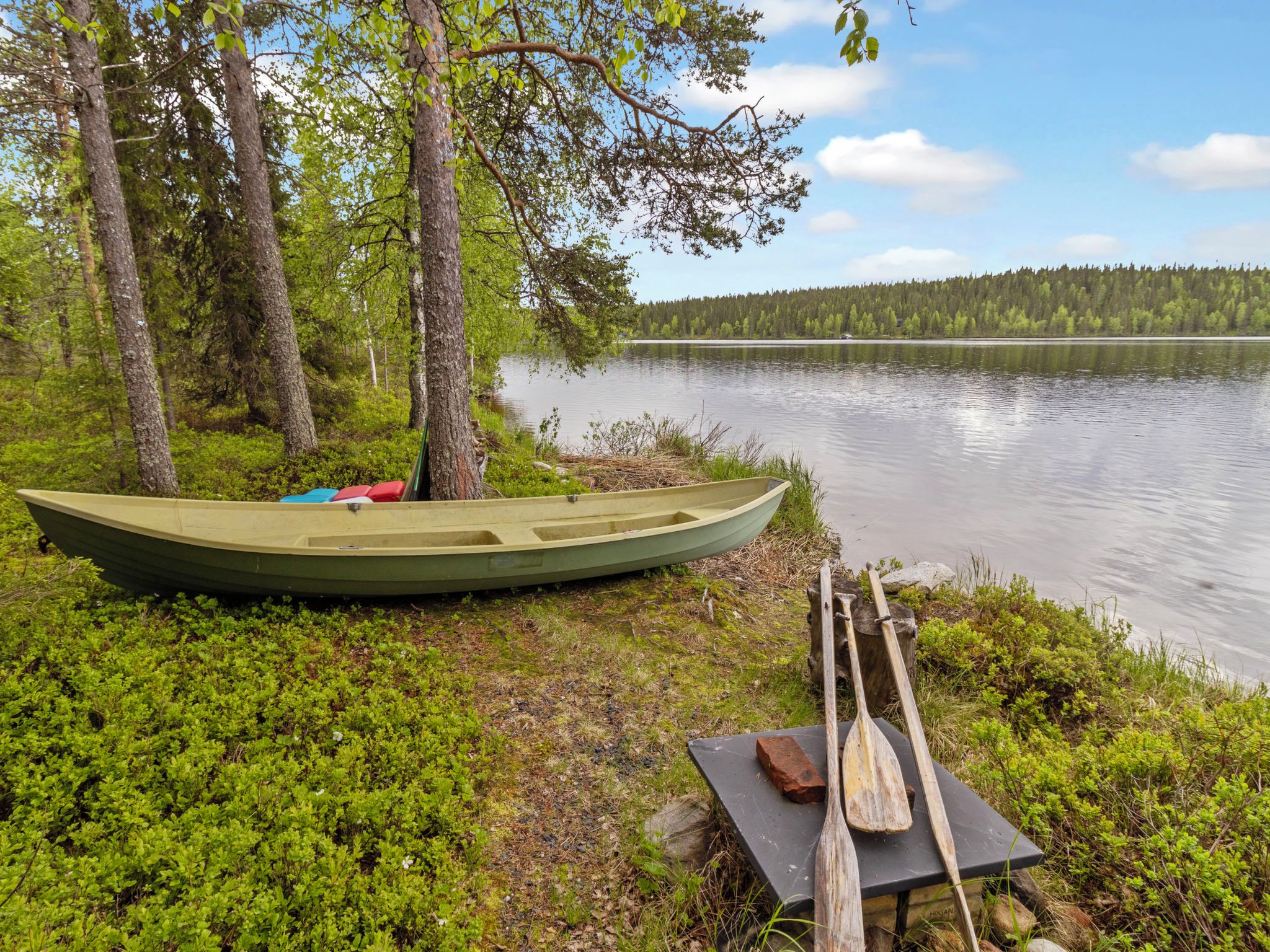 A canoe tied to a tree by a calm lake with a forest in the background.