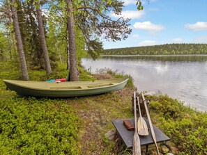 Un canoë est attaché à un arbre au bord d’un lac paisible, avec une forêt en arrière-plan.