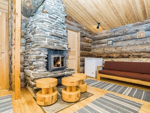 A log cabin interior with a stone fireplace, wooden furniture, and a cozy seating area.