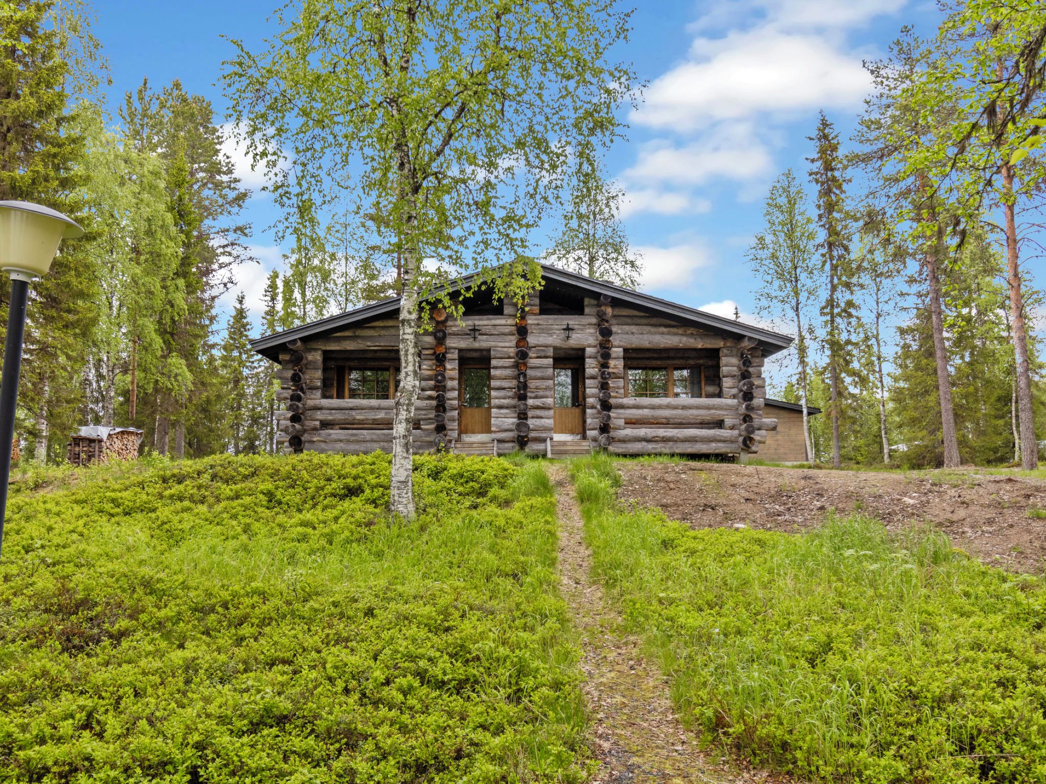 Une cabane en rondins dotée d’un porche, entourée de verdure et d’arbres.