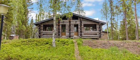 Une cabane en rondins dotée d’un porche, entourée de verdure et d’arbres.