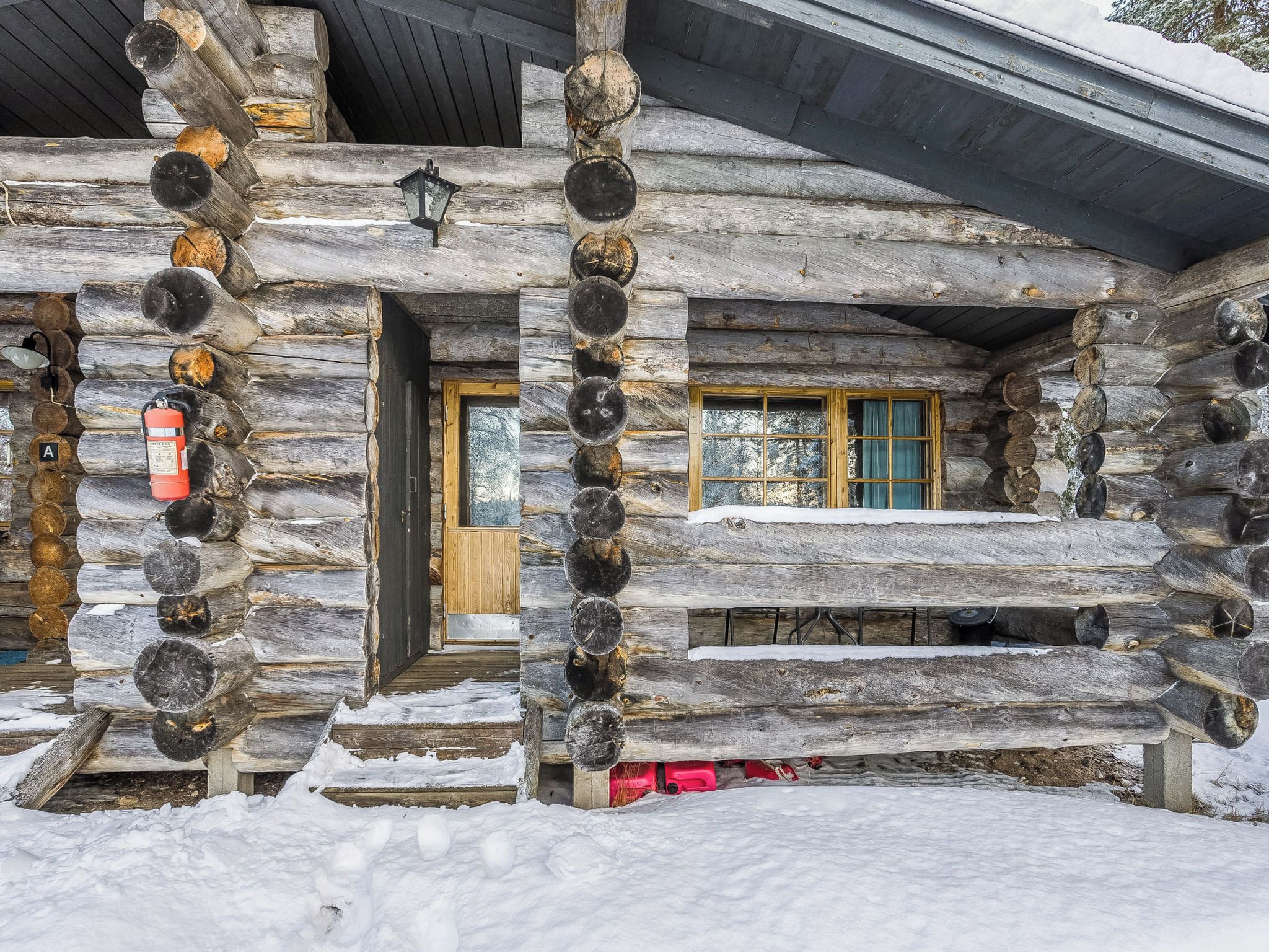 A log cabin with a wooden door, a window with curtains, and a fire extinguisher mounted on the wall.