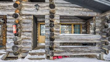 A log cabin with a wooden door, a window with curtains, and a fire extinguisher mounted on the wall.