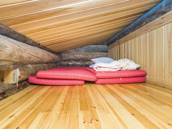 Un intérieur en bois avec un plafond en pente, un mur en pierre et un lit avec une literie rouge.