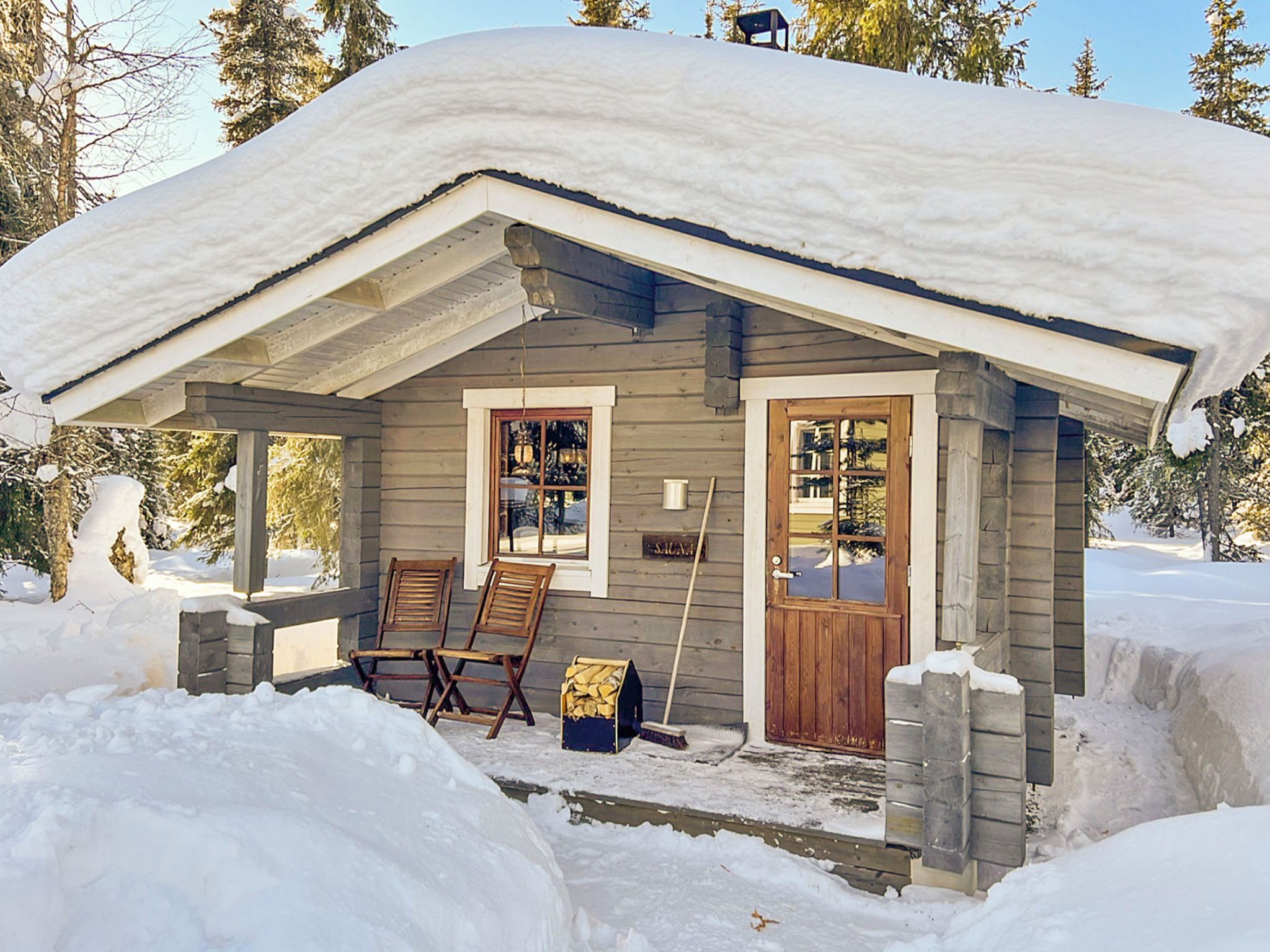 Une cabane en bois avec un toit enneigé, deux fenêtres et une porte.