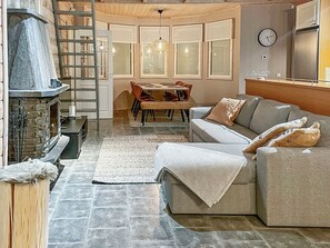 A cozy living room with a stone fireplace, a dining area with a table and chairs, and a sofa with cushions.