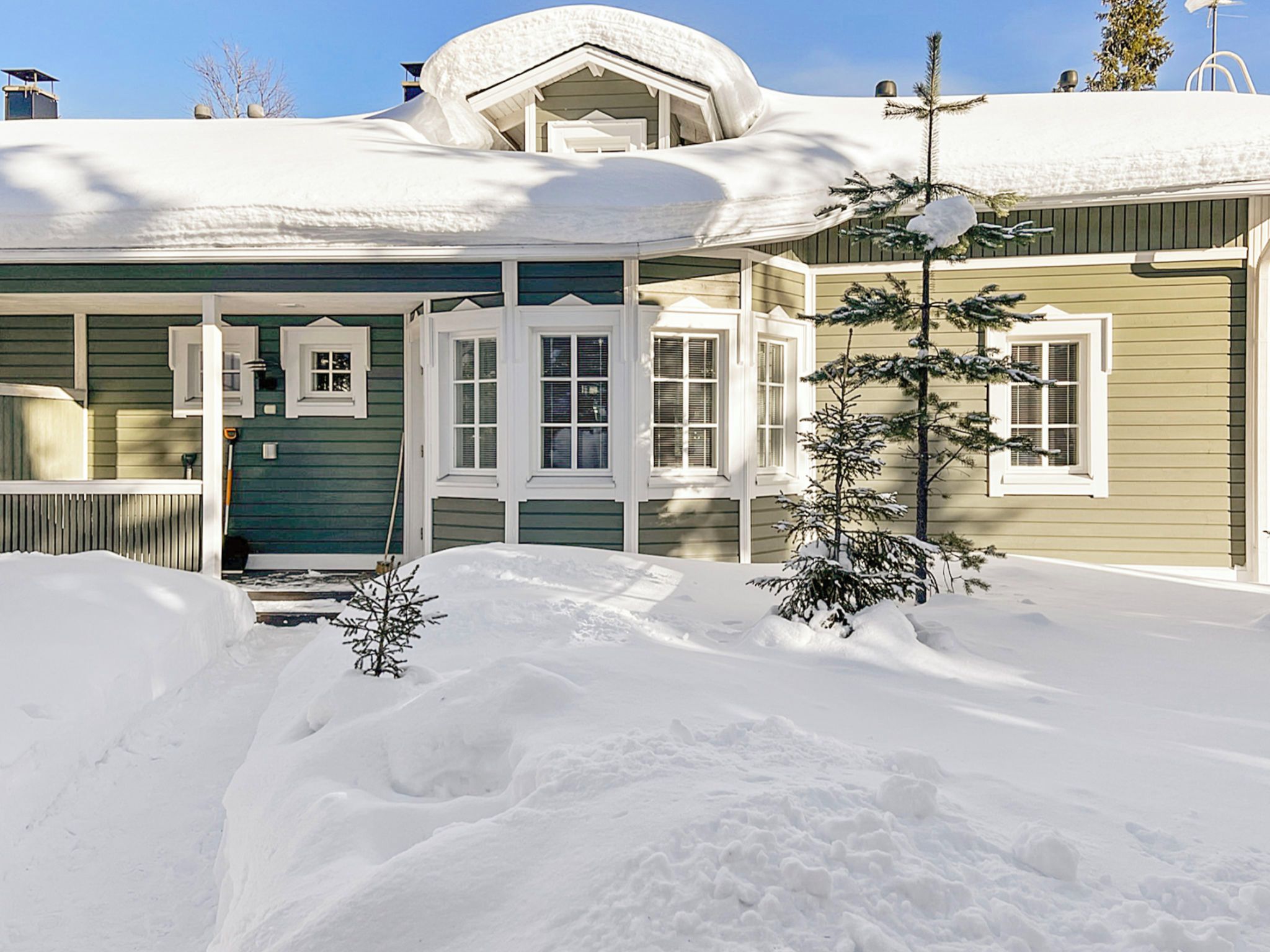 Ein mit Schnee bedecktes Haus mit Veranda und einem kleinen Baum.