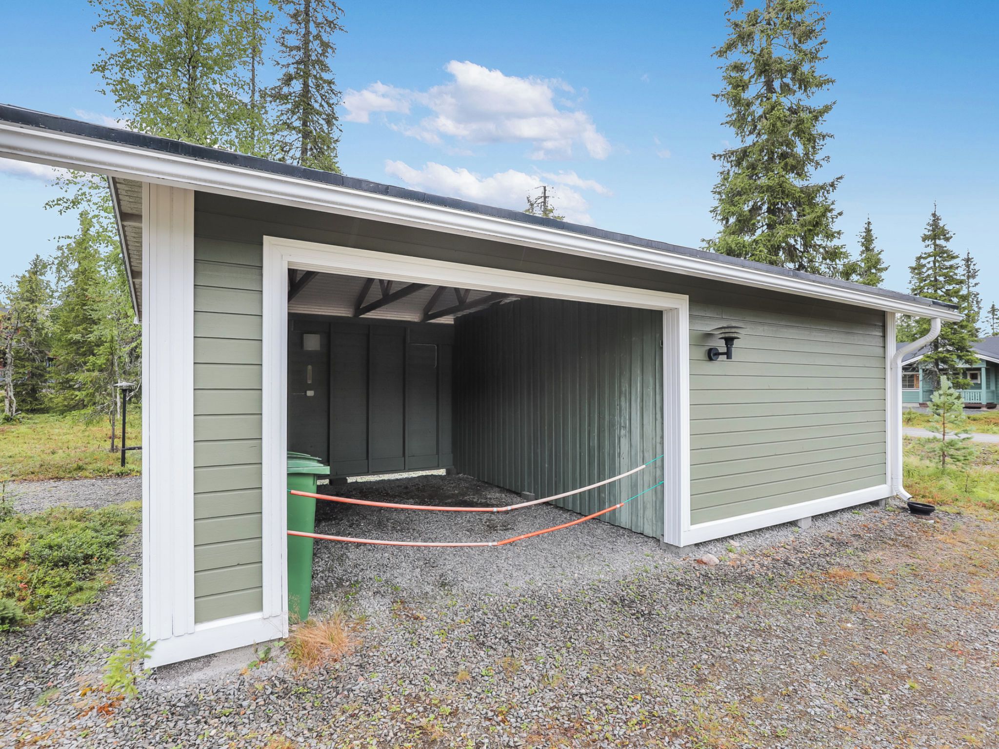 A single-story building with a covered garage area, a green exterior, and a gravel driveway.