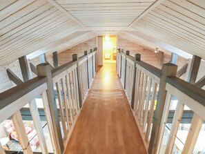 A wooden staircase with a railing leading to a room with a window and a light source.