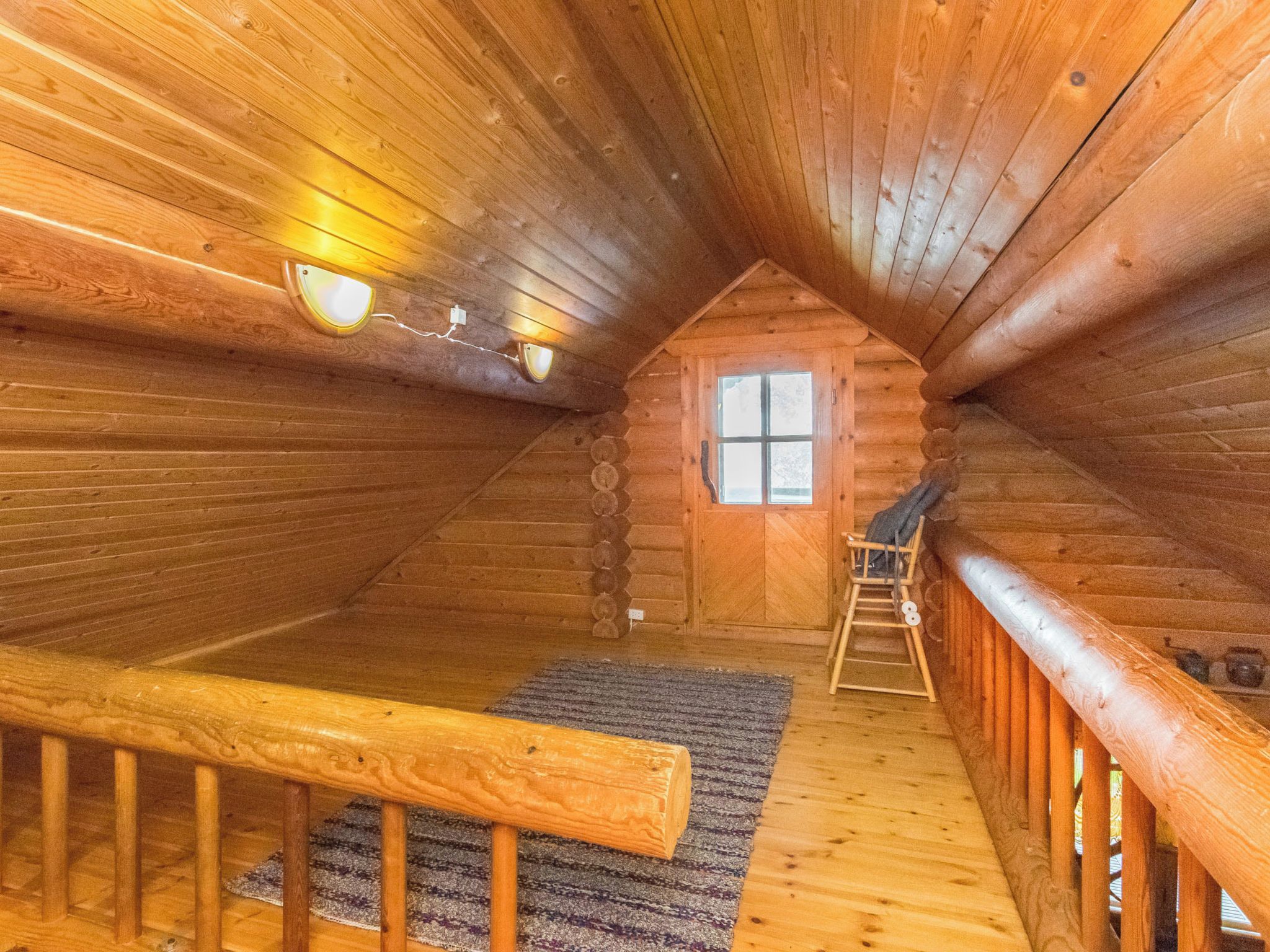 Ein Holzblockhaus-Interieur mit einer Holztreppe, einem Fenster und einem kleinen Holzstuhl.