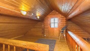 Ein Holzblockhaus-Interieur mit einer Holztreppe, einem Fenster und einem kleinen Holzstuhl.