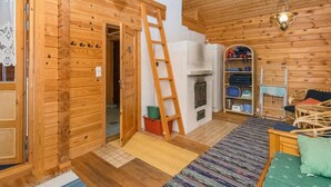 A wooden cabin interior with a loft bed, a ladder, a fireplace, and a storage area with shelves.