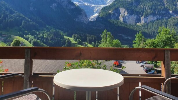 En balkong med ett bord och stolar, med utsikt över ett bergigt landskap, och en parkeringsplats syns på förgrunden.