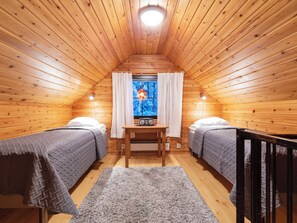 Une chambre confortable située dans les combles, avec des murs en bois, une fenêtre avec des rideaux, deux lits, une table et un tapis.