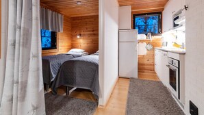 Una cabaña pequeña con interior de madera, una cama, un kitchenette y una ventana con vistas.