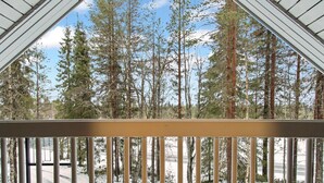 Una terraza de madera con barandilla que da a un paisaje nevado y altos árboles.
