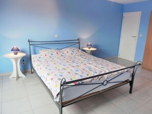 Une chambre à coucher avec un lit en métal, une couvre-lit à motifs, deux tables de chevet avec des lampes et une porte.