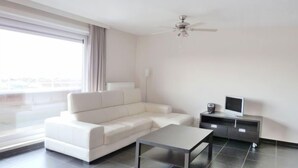Un soggiorno moderno con un divano bianco, un tavolino da caffè, una TV su un mobile basso e una ventola a soffitto.
