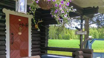 Una cabaña de troncos con un banco de madera, una cesta de flores colgante y una puerta con un tirador decorativo.